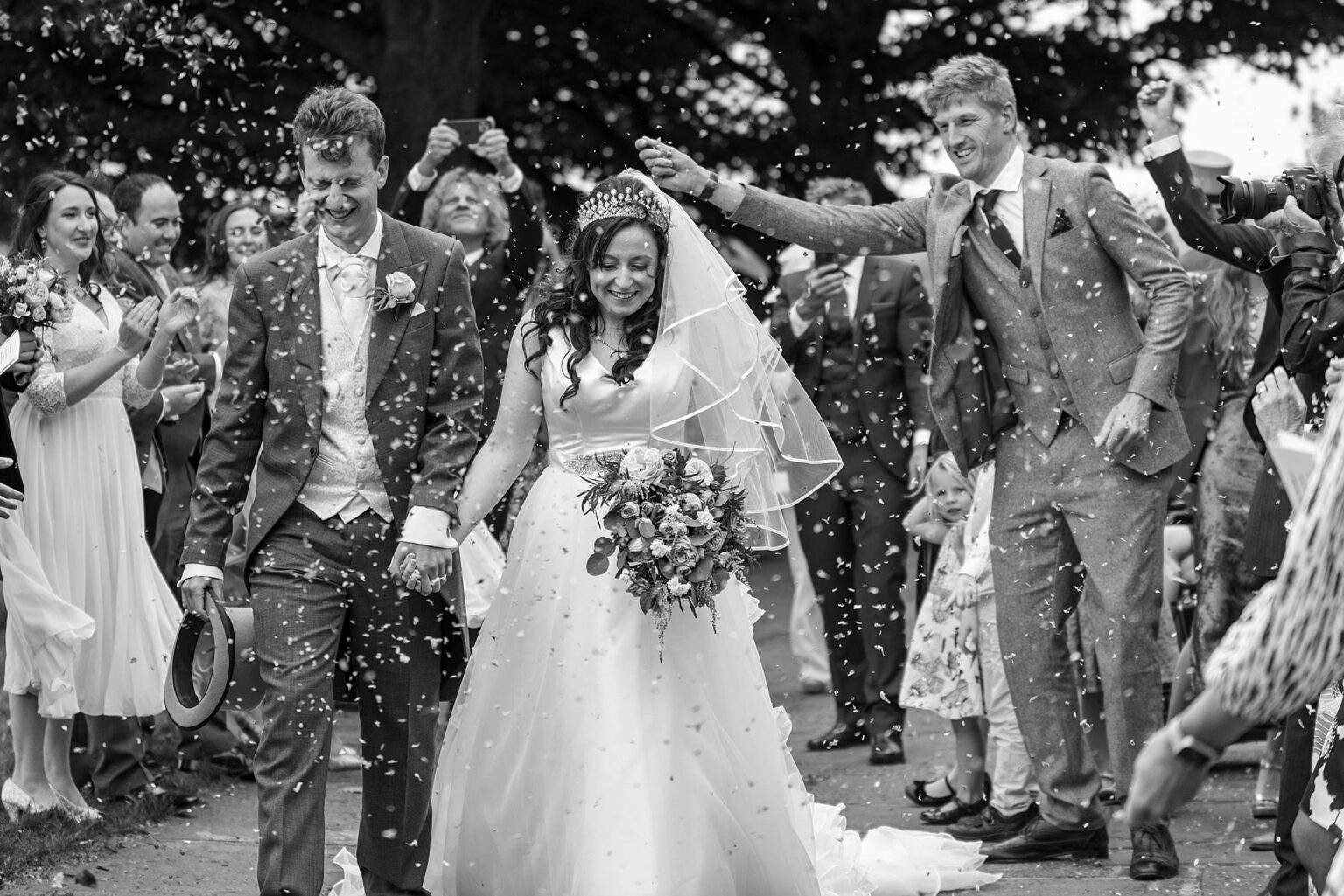 bride and groom walk through a confetti tunnel as dad is busy throwing it behind them